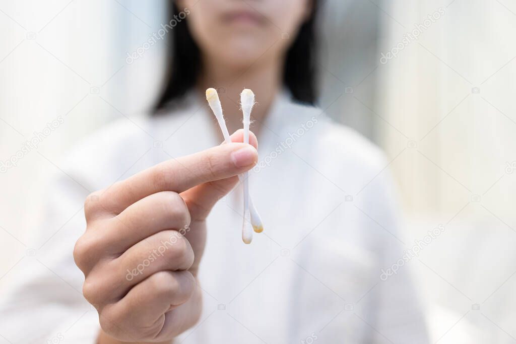 Close up,Hand of asian child girl holding cotton bud with a lot of ear wax or wet cerumen after cleaning her ear canal with cotton swab,removing earwax from ears,health care,hygiene,lifestyle concept