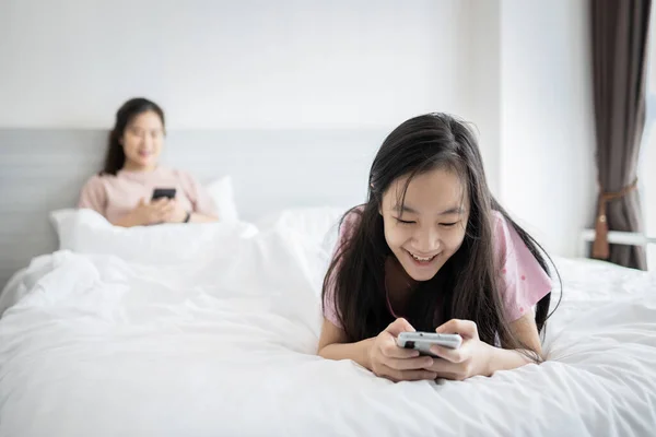 亚洲的孩子女儿用手机打字发短信 和妈妈在床上聊天 沉迷于手机 上网聊天 上网成瘾 — 图库照片