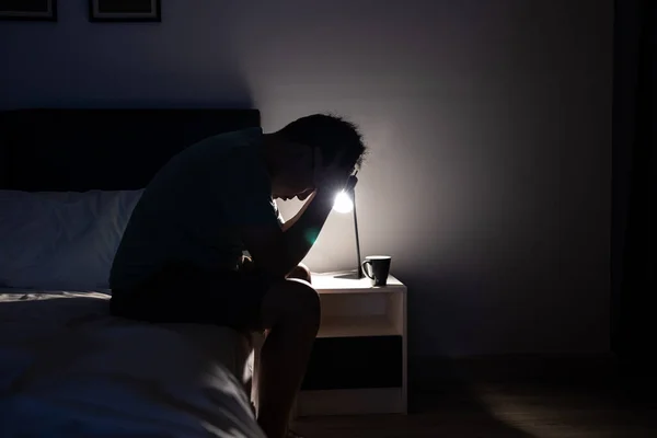 Depressed asian man crying covering face with his hands,sitting on the bed at night,Stressed worried people touching his head,suffering from grief sorrow insomnia,feel anxiety,trouble of mental health