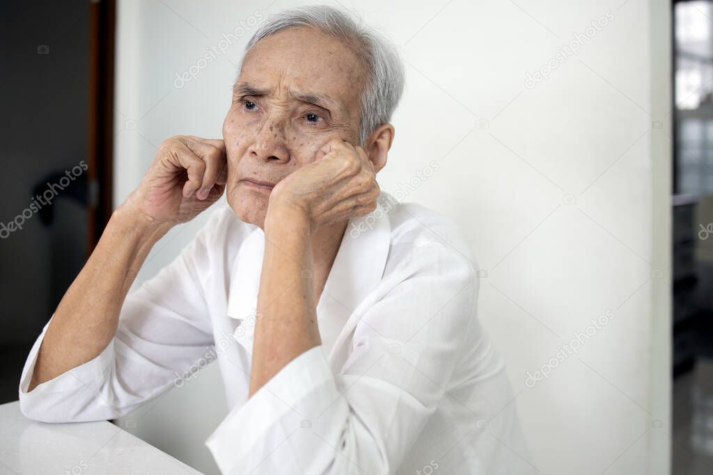Bored senior woman is propped her cheeks with hands,sad facial expression,spending home alone,asian elderly people thinking having question feeling weary or lacks interest in the care from her family