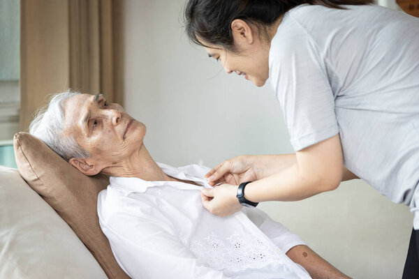 Asian female caregiver taking care of helping elderly patient get dressed,button on the shirt or changing clothes for a paralyzed person,senior woman with paralysis of limbs,body or muscles weakness