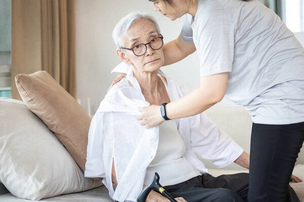 Assisting in dressing,asian female caregiver taking care of helping senior woman get dress,chang clothes for old mother,Alzheimer's elderly patient sit on the sofa at home,preparing go to the hospital