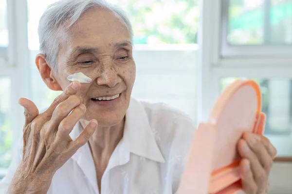 快乐微笑的亚洲老年妇女在脸颊上涂防晒霜 保护她美丽的脸庞 老年老人用护肤产品处理敏感的皮肤 在阳光充足的日子在脸上涂防晒霜 — 图库照片