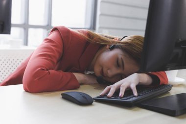 Kırmızı üniformalı Asyalı kadın çağrı merkezi operatörü işten yorgun hissediyor ve ofiste uyuyor. Müşteri desteği konsepti, iş yerinde yaşam tarzı, çalışan.
