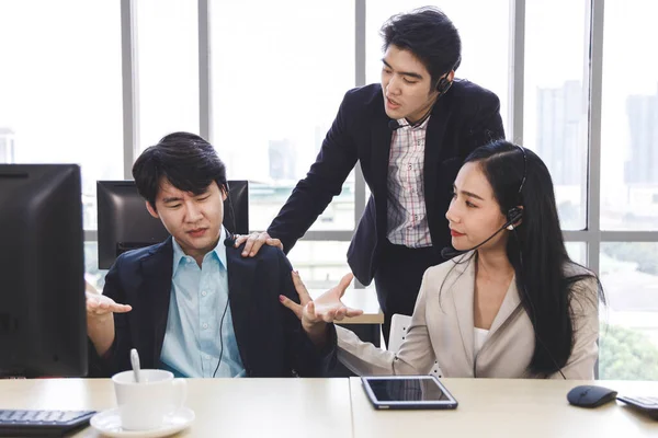 Two Asian call center agents cheer their colleague up who has problem about his work, project or personal life.