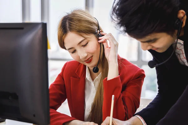 Two Asian call center operator agents working together and help each other. Concept for business, teamwork, office lifestyle.