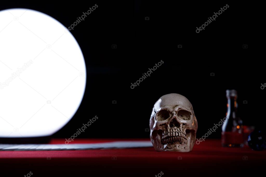Skull on fortune teller's table with bright crystal ball on the left side.