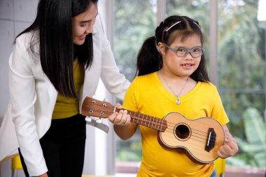 Asyalı öğretmen Down sendromlu bir kıza ukulele öğretiyor. Okulda engelli çocuk öğrenimi kavramı.
