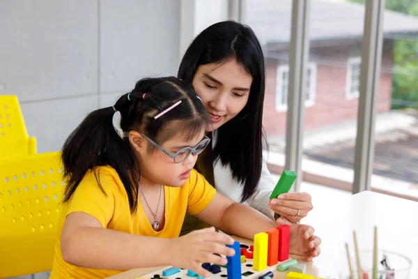 アジアの女の子とともにダウンの症候群遊びパズルおもちゃとともに彼女の先生で教室 — ストック写真