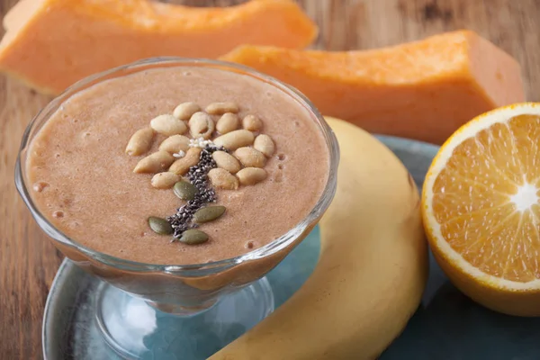 Pumpkin smoothies with banana and orange in a glass bowl on a turquoise plate