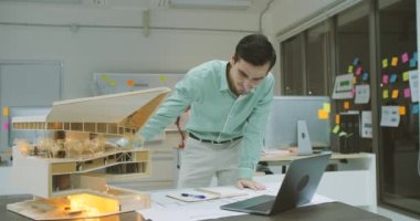 Genç emin beyaz erkek mimar çalışma gece ofiste bir mimari modeli.