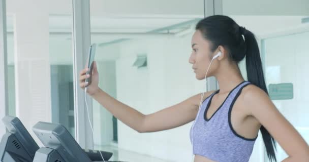 Asijská dívka běží na běžeckém pásu a mluví o telefonu. — Stock video