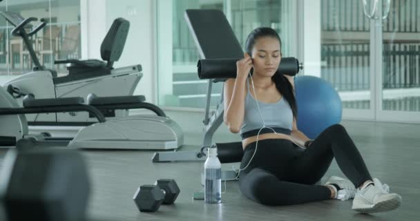 Joven mujer deportiva escuchando música en el teléfono inteligente en el gimnasio . — Vídeo de stock