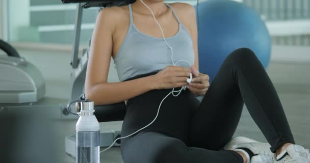 Junge sportliche Frau hört im Fitnessstudio Musik auf dem Smartphone. — Stockvideo