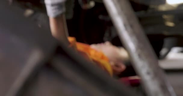 Junge schöne Automechaniker liegt unter dem Auto, um es zu reparieren. — Stockvideo