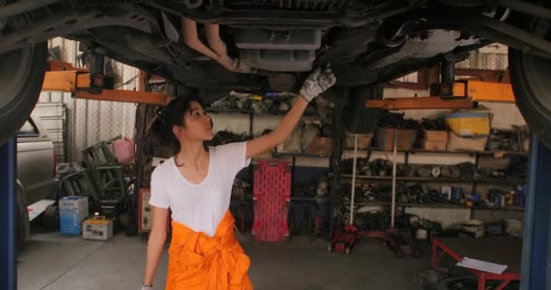 Jovem lindo carro mecânico inspeciona o carro undercarriage maneira na garagem . — Vídeo de Stock