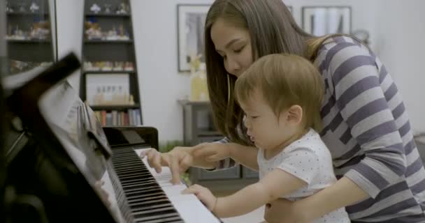 Молодая азиатская мать играет на пианино со своим малышом . — стоковое видео