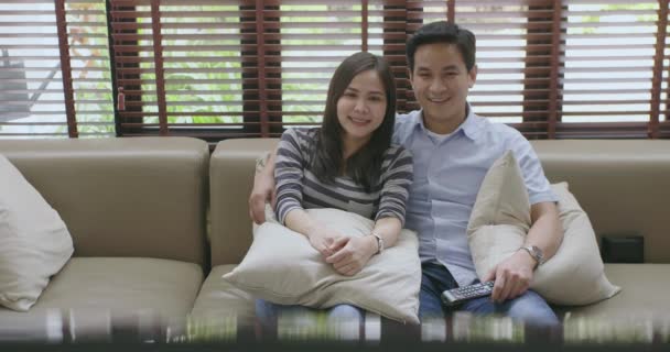 年轻的亚洲情侣看电视拥抱在新房子的沙发上, 一起看电影. — 图库视频影像