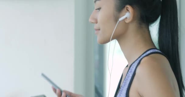 Asiatisk flicka kör på löpbandet i gymmet med hörlurar. — Stockvideo