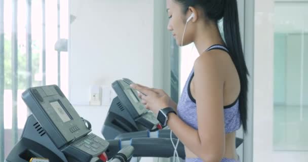 Aziatisch meisje draait op de loopband in de sportschool met koptelefoon. — Stockvideo