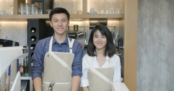 Retrato de dos jóvenes baristas asiáticos hombre y mujer cruzando las manos y sonriendo en la cámara en la cafetería — Vídeos de Stock