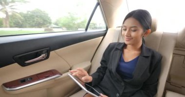 Genç Asyalı işkadını arkada arabanın koltuğuna oturan pc tablet kullanır.