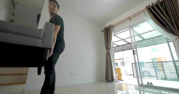 Feliz jovem asiático casal movendo um sofá no novo apartamento . — Vídeo de Stock