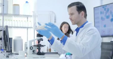 Tıbbi araştırma bilim adamları laboratuvar fare bir kafeste bakarak. Laboratuvar parlak ve Modern