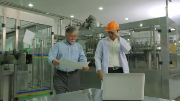 Directeur principal avec ouvrier mécanique vérifiant les plans de production avec ligne de production de bouteilles en arrière-plan . — Video