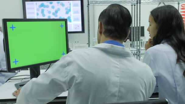 Два медицинских исследователя смотрят на зеленый экран в современной лаборатории — стоковое видео