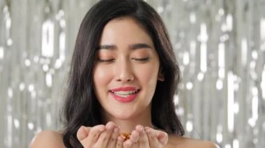 Güzel Asyalı kadın altın glitter konfeti üfleme.