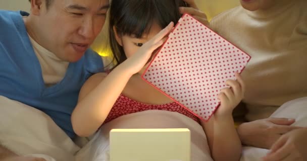 開く誕生日プレゼントし、ベッドに喜ぶ娘を祝う幸せなアジア家族. — ストック動画
