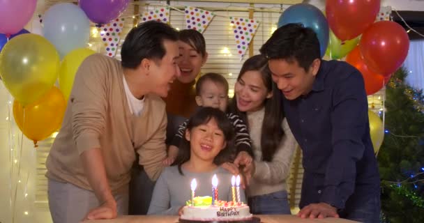 Roztomilá malá Asijská dívka sedí u stolu a foukání svíčky na narozeninový dort, zatímco její rodina stojí za a zpívat píseň k ní. — Stock video