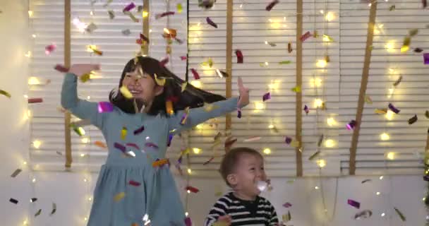 Двоє дітей грають з конфетті і весело стрибають у вітальні — стокове відео