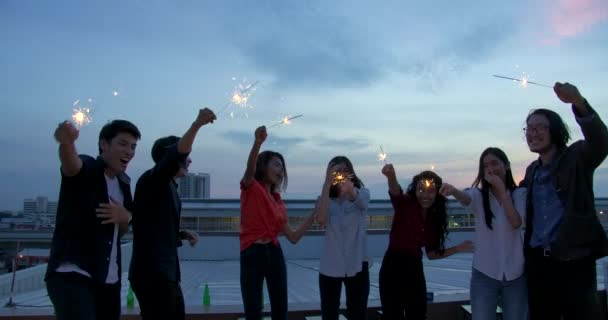 Eine fröhliche Gruppe junger Freunde genießt und spielt Wunderkerzen bei einer Party auf dem Dach bei Sonnenuntergang. Feiertagsfeier festliche Party. Teenager-Lifestyleparty. — Stockvideo