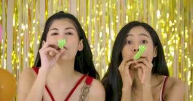 İki kız ağır çekimde parti boynuz üfleyici ile eğleniyor.