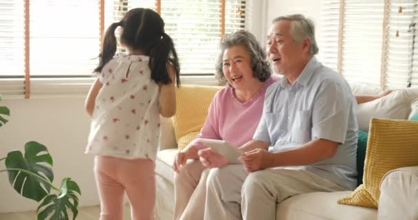 Meisje komt te omhelzen haar grootvader en grootvader terwijl ze spelen tablet. Kind spelen met senior man en vrouw met gelukkig emotie. — Stockvideo