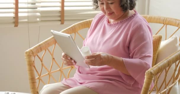 Asiatische Seniorin hält Drogenflasche in der Hand und sucht Informationen darüber. — Stockvideo