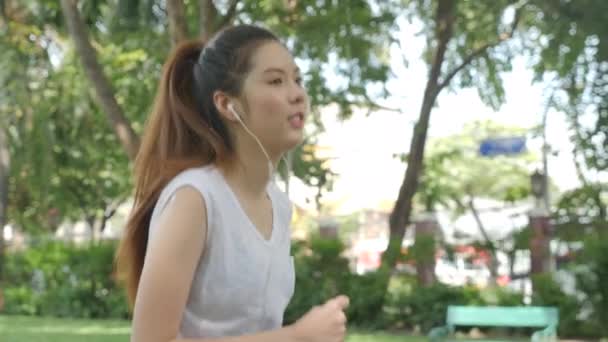 Young attractive woman listening music in the earphone while running in the green city park. — Stock Video