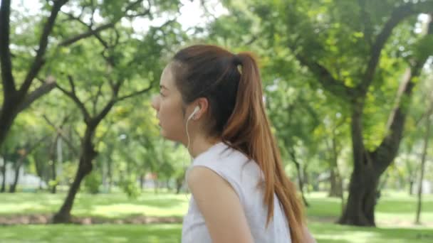 Mujer atractiva joven escuchando música en el auricular mientras se ejecuta en el parque verde de la ciudad . — Vídeos de Stock