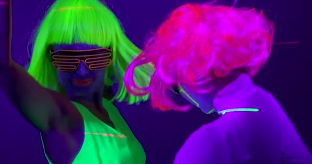 Långsam motin vackra sexiga kvinnor med fluorescerande make-up och kläder dans i neon ljus. — Stockvideo