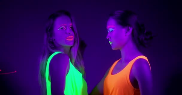 Повільна монета красивих сексуальних жінок з флуоресцентним макіяжем та одягом, що танцює в неоновому світлі . — стокове відео