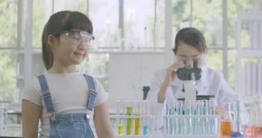 Arka planda çalışan kadın bilim adamı ile kimya laboratuarında kameraya gülümseyen bir Asyalı Kız portresi