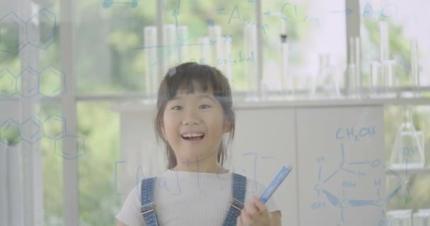 Piccola studentessa asiatica che scrive "Scienza" sulla lavagna di vetro trasparente . — Video Stock
