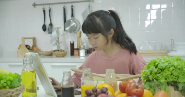Liten asiatisk flicka söker sallad recept på digitala tabletten medan matlagning en måltid i köket hemma — Stockvideo
