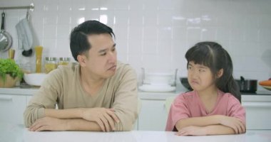 Misunderstanding between upset father and daughter, dad and kid sitting at table and cross their own arm with sulking and touchy in the kitchen