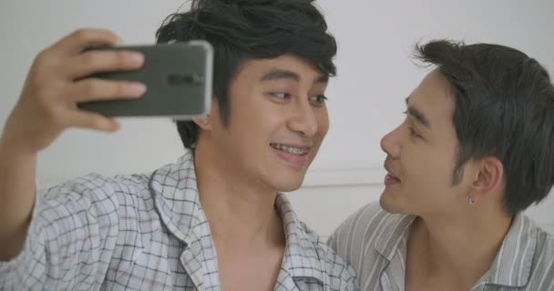 Młode Azjatki pary gejów siedzi na łóżku przytul i przy użyciu telefonu biorąc selfie sypialnia razem w domu. — Wideo stockowe