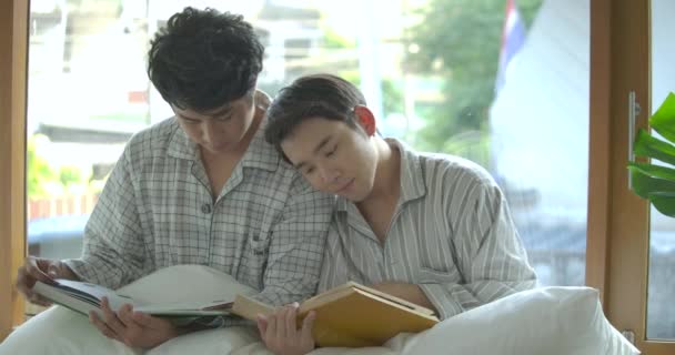 Les jeunes asiatique gay couple assis sur l 'fenêtre seuil et lecture livre à la maison dans l' matin — Video