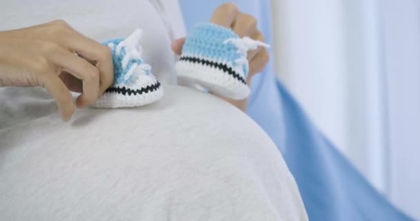 Έγκυος γυναίκα παίζει με τα μικρά παπούτσια στην κοιλιά της για το αγέννητο μωρό στο κρεβάτι. — Αρχείο Βίντεο