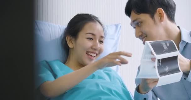 Adorável asiático casal animado pais-a-ser olhar para imagens de ultra-sonografia — Vídeo de Stock
